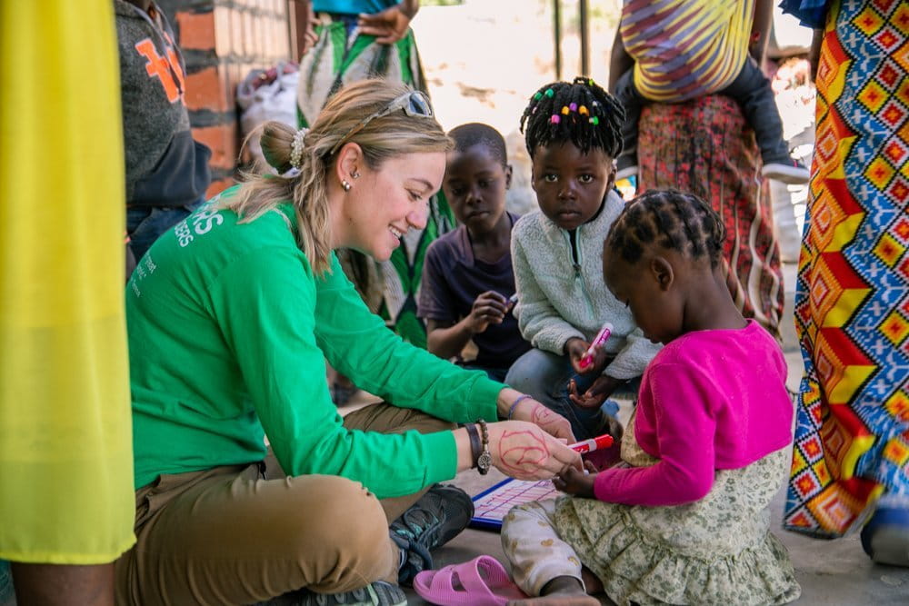 Expeditions volunteer in Zambia sitting on the ground and painting nails with little girls in Zambia.