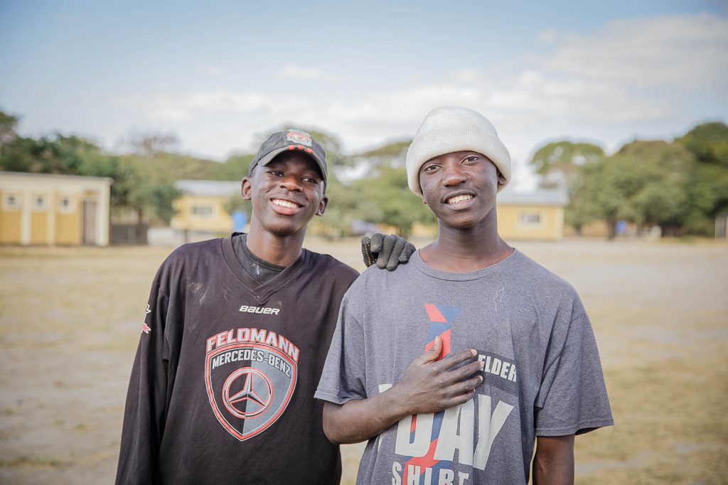 Zambian teen boys standing next to each other and smiling outside.